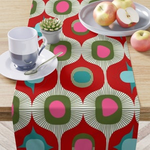 May include: Red table runner with a geometric pattern of green, pink, and blue circles. The pattern is repeated throughout the runner.