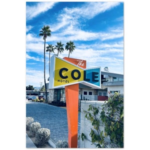 Puede incluir: Un cartel colorido para el Hotel The Cole con un esquema de colores amarillo, azul y naranja. El cartel tiene forma de pajarita y tiene las palabras "The Cole Hotel" en letras negras.