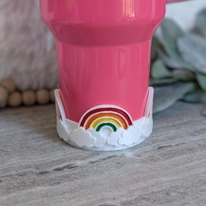 May include: Pink tumbler with a white rainbow and cloud design on the bottom.