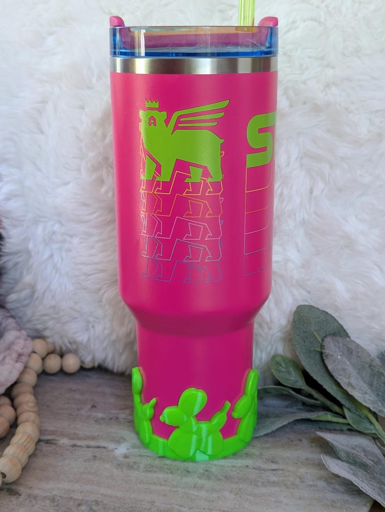 May include: A pink insulated tumbler with a green winged bear graphic and the number 5. The tumbler has a green cactus-shaped base and a blue lid with a green straw. The tumbler is designed to keep drinks cold or hot.