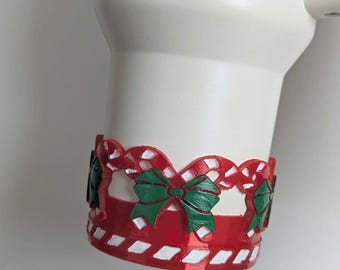 May include: A white tumbler with a red and white candy cane and green bow Christmas themed wrap around the bottom.