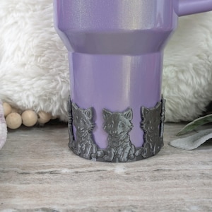 May include: A purple travel mug with a silver glitter finish and a black metal band with three wolf figurines around the bottom.