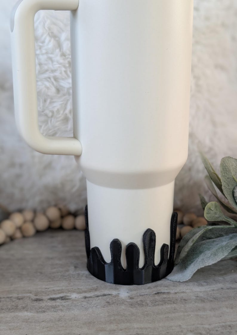 Puede incluir: Una taza de viaje blanca con un dise&ntilde;o de goteo negro alrededor de la parte inferior. La taza tiene un asa y una tapa.