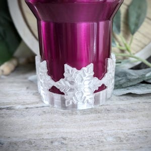 May include: A close-up of a purple tumbler with a white snowflake-shaped silicone base.