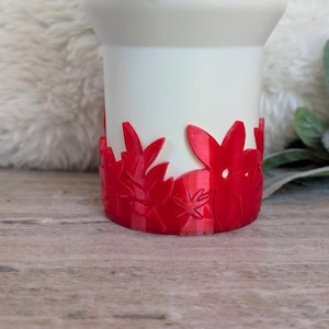 May include: White ceramic candle holder with a red floral design around the base.