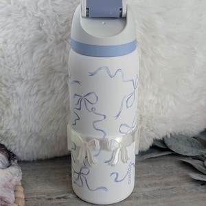 May include: White water bottle with a blue lid and a blue and white ribbon design. The bottle has a white ribbon around the middle with a bow on each side.