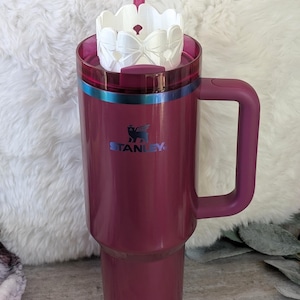 May include: A burgundy stainless steel travel mug with a handle and a white lid with a straw. The mug has the Stanley logo on the front.