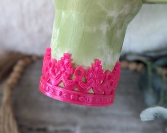 May include: A green and white patterned tumbler with a pink crown-shaped base.