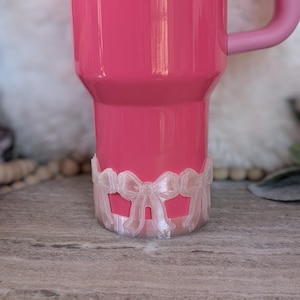 Puede incluir: Un vaso rosa con un anillo de plástico blanco en forma de lazo alrededor de la base.