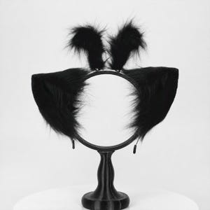 May include: A black headband featuring two large, pointed, faux fur cat ears attached to the sides and two smaller, upright, fluffy faux fur tufts positioned at the top center of the thin, circular black band frame.