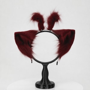 May include: A dark burgundy headband featuring two large, pointed, faux fur animal ears on the sides and two smaller, upright, tufted faux fur accents at the top. The headband is constructed from a thin, circular black frame.