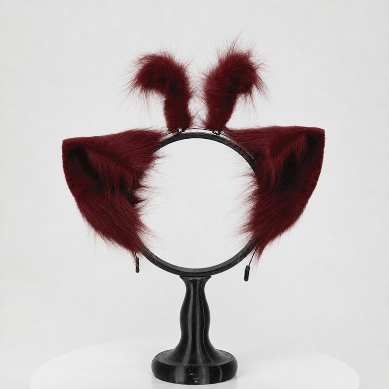 May include: A dark burgundy headband featuring two large, pointed, faux fur animal ears on the sides and two smaller, upright, tufted faux fur accents at the top. The headband is constructed from a thin, circular black frame.