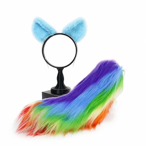 May include: A set consisting of a black headband with two light blue faux fur ears and a long, plush, multi-colored faux fur tail featuring a vibrant rainbow gradient pattern of red, orange, yellow, green, blue, and purple synthetic fibers.
