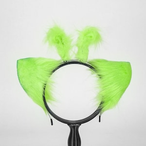 May include: A black headband featuring two large, pointed, neon green faux fur ears attached to the sides and two smaller, upright, neon green faux fur tufts positioned at the top center, creating a textured and vibrant appearance.