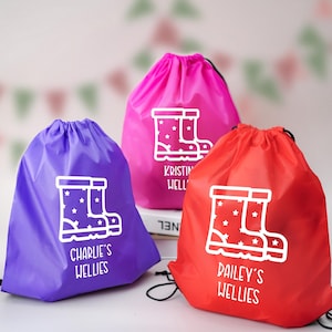 May include: Three drawstring bags in purple, pink, and red. Each bag has a white graphic of wellington boots with stars and a name below. The purple bag says "Charlie's Wellies", the pink bag says "Kristin Well", and the red bag says "Pailey's Wellies".