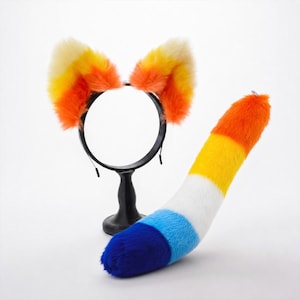 May include: A black headband featuring two faux fur ears with a gradient of cream, yellow, and orange. Beside it lies a plush faux fur tail with horizontal stripes of orange, yellow, white, light blue, and dark blue, ending in a rounded tip.