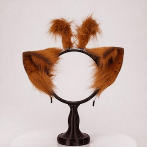 May include: A black headband featuring two large, pointed, brown faux fur animal ears on the sides and two smaller, upright, tufted brown faux fur accents on the top. The ears have dark brown shading and small dot patterns near the outer edges.