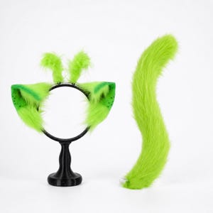 May include: A bright lime green faux fur costume set consisting of a headband with two large pointed ears and two smaller tufted antennae, alongside a long, curved, matching lime green faux fur tail with a small silver attachment loop.