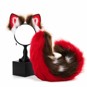 Op de afbeelding: Een set bestaande uit een haarband met twee dierenoren van imitatiebont en een bijpassende lange staart van imitatiebont. De oren en staart hebben een kleurenpalet van felrood, donkerbruin en wit, met witte details aan de binnenkant van de oren.