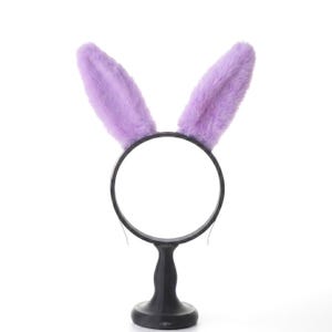 Könnte beinhalten: Ein schwarzes Stirnband mit zwei aufrechten, flauschigen, lavendelfarbenen Hasenohren. Die Ohren bestehen aus einem weichen, plüschigen Material. Das Stirnband wird von einem schwarzen Ständer getragen, was ein skurriles und verspieltes Accessoire ergibt.
