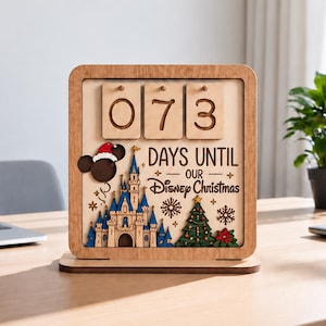 May include: A square wooden countdown calendar featuring the text 073 DAYS UNTIL OUR Disney Christmas. The design includes a layered wooden castle, a decorated Christmas tree, snowflakes, and a Mickey Mouse icon wearing a red Santa hat.