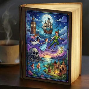 Peut inclure: Une lampe rectangulaire en bois en forme de livre présentant une illustration style vitrail de Peter Pan, Wendy, John, Michael et la fée Clochette volant vers un navire pirate, avec Big Ben, un rocher crâne, des sirènes et un feu de camp.