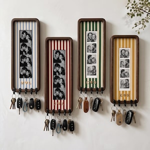 May include: Four rectangular wooden wall-mounted key holders with vertical striped backings in blue, red, green, and yellow. Each frame displays a vertical strip of four black and white photos and features four black hooks holding various keys.