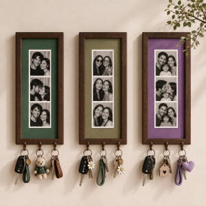 Op de afbeelding: Drie rechthoekige wand-sleutelhouders van donker hout met fotolijsten. Elke lijst toont een verticale strook van drie zwart-witfoto's op een groene, olijfkleurige en paarse achtergrond. Elke houder is voorzien van drie metalen haken voor sleutels.