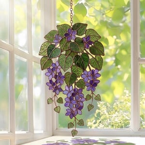 Pu&ograve; includere: Appeso per finestra in vetro colorato raffigurante un grappolo di fiori viola e foglie verdi. Il disegno floreale &egrave; sospeso a una catena e appeso davanti a una finestra. Il vetro &egrave; delineato con un materiale color rame.