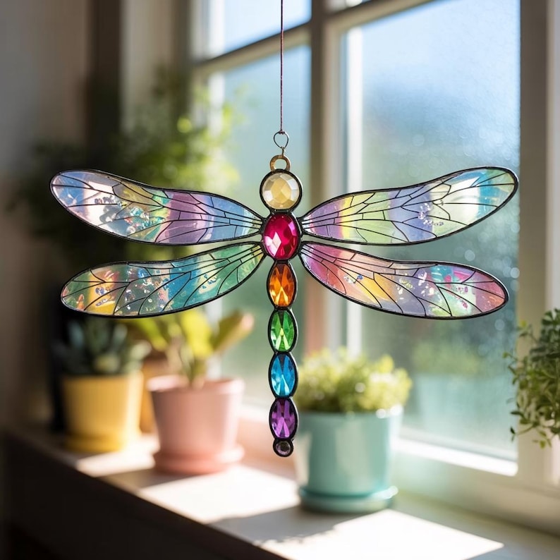 May include: A colorful stained glass dragonfly suncatcher. The dragonfly features iridescent wings with rainbow hues and a body adorned with jewel-toned gems. The suncatcher is suspended by a thin wire, perfect for hanging in a window.