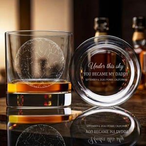 Puede incluir: Un vaso de whisky transparente con un diseño de constelación y líquido ámbar. Junto a él, un posavasos con la inscripción "Under this sky YOU BECAME MY DADDY SEPTEMBER 6, 2026 | POWAY, CALIFORNIA".