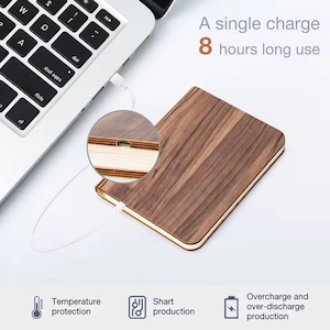 May include: A wooden-look, book-shaped device is connected to a laptop via a white cable. The device is brown with a wood grain pattern. Text on the image reads: "A single charge 8 hours long use". Additional icons indicate temperature protection, short production, and overcharge protection.