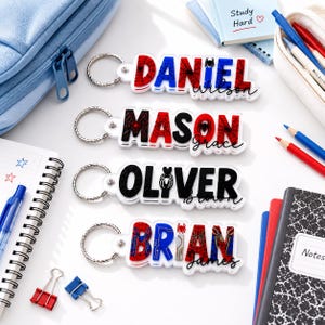 May include: Four custom acrylic keychains featuring the names Daniel, Mason, Oliver, and Brian in bold, block lettering. Each keychain includes a metal ring and a spider-themed graphic design with red, blue, and black colors, plus a secondary name in script.