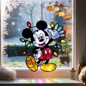 Puede incluir: Decoración de ventana de Mickey Mouse con un diseño festivo. El personaje en blanco y negro está rodeado de luces de colores. Mickey lleva pantalones cortos rojos y zapatos amarillos. La decoración cuelga frente a una ventana con una escena invernal.