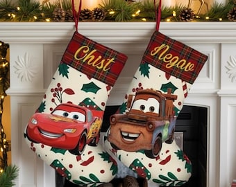 Op de afbeelding: Twee kerstsokken met rode geruite bovenkanten en de namen "Chist" en "Negav" in goud geborduurd. De sokken hebben afbeeldingen van Bliksem McQueen en Takel uit de film Cars, met een crèmekleurige achtergrond en een hulst- en bessenpatroon.