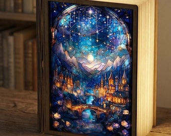 May include: A rectangular book-shaped lamp with a wooden frame and illuminated pages. The front cover features a vibrant stained-glass style illustration of a castle, a stone bridge, and a starry night sky with a bright moon over mountains.