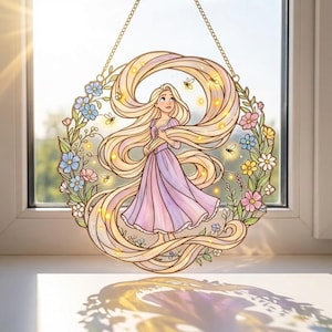 Peut inclure: Décoration de fenêtre en vitrail représentant une princesse aux longs cheveux blonds et une robe lavande, entourée d'une couronne florale. Le design comprend de petites lumières et est suspendu par une chaîne dorée. L'œuvre est placée devant une fenêtre.