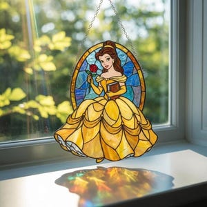 K&ouml;nnte beinhalten: Ein ovaler Buntglas-Sonnenf&auml;nger mit einer weiblichen Figur mit braunem Haar in einem gelben Kleid, die eine rote Rose und ein braunes Buch h&auml;lt. Der Hintergrund besteht aus blauen Glassegmenten. Das St&uuml;ck h&auml;ngt an einer silbernen Metallkette.