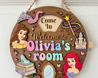 Può includere: Un cartello rotondo in legno con la scritta "Come In" e "Welcome to Olivia's room". Il cartello presenta illustrazioni di una principessa, un castello, una bacchetta magica, una scarpetta di cristallo e uno specchio. Il cartello è marrone con accenti colorati.