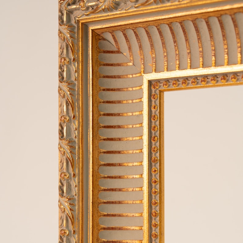 May include: Close-up of a decorative picture frame with a gold and off-white color scheme. The frame features ornate detailing, including a gold inner border and a textured, ribbed design on the off-white sections. The frame's corner is visible.