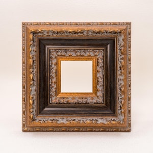 Op de afbeelding: Vierkante fotolijst met een gelaagd ontwerp. Het frame heeft een goud- en bruine afwerking met sierlijke details. Het binnenste frame is zwart en het binnenste frame is goud.