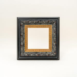 May include: Square picture frame with a black exterior, gold interior, and ornate floral detailing. The frame is empty, ready to display a photograph or artwork. The frame's dimensions are approximately 20 cm by 20 cm.