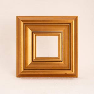 Op de afbeelding: Een vierkante fotolijst met een metallic gouden afwerking. De lijst heeft een meerlaags, getrapt profiel dat schuin afloopt naar de opening in het midden. Het oppervlak heeft een gladde, gepolijste uitstraling met subtiele variaties in de goudtint.