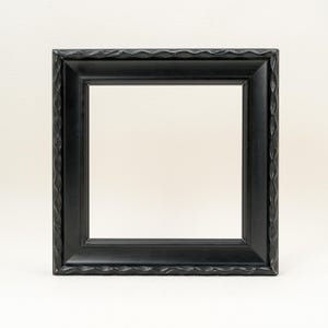 May include: A square picture frame with a matte black finish. The frame features a smooth inner border and an outer edge decorated with a repeating, wave-like carved pattern. The design is symmetrical, providing a clean, dark border for display.