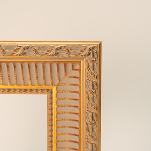 May include: Close-up of a decorative picture frame with a gold and silver finish. The frame has ornate detailing along the edges, with a repeating pattern of leaves and floral elements. The inner portion of the frame is a light beige color.
