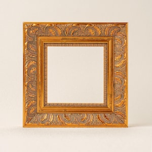 Może przedstawiać: Kwadratowa, ozdobna rama do zdjęć ze złotym wykończeniem. Rama ma szczegółowe, wypukłe wzory reliefowe i ciepłą, antyczną estetykę. Wewnętrzna rama ma jaśniejszy złoty kolor, tworząc efekt warstwowy. Rama jest pusta.