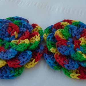May include: Two crocheted flower shapes in red, yellow, blue, and green. The flowers are made of yarn and have a layered, multi-dimensional appearance.