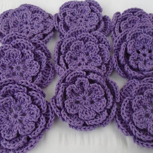 May include: A collection of nine crocheted purple flowers. The flowers are made with a single crochet stitch and have a five-petal design.