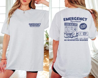 May include: A light gray t-shirt with the words "EMERGENCY DEPARTMENT" printed in navy blue on the front and back. The back of the shirt features a navy blue graphic of a cafe with the text "CODE BLUE CAFE" and "OPEN 24/7".