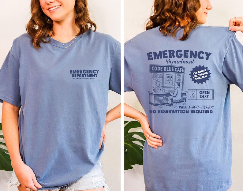 May include: A dusty blue t-shirt with the words "EMERGENCY DEPARTMENT" printed on the front. The back of the shirt features a graphic of a cafe with the text "CODE BLUE CAFE", "ASK ABOUT OUR TRAUMA SPECIALS!", and "OPEN 24/7".